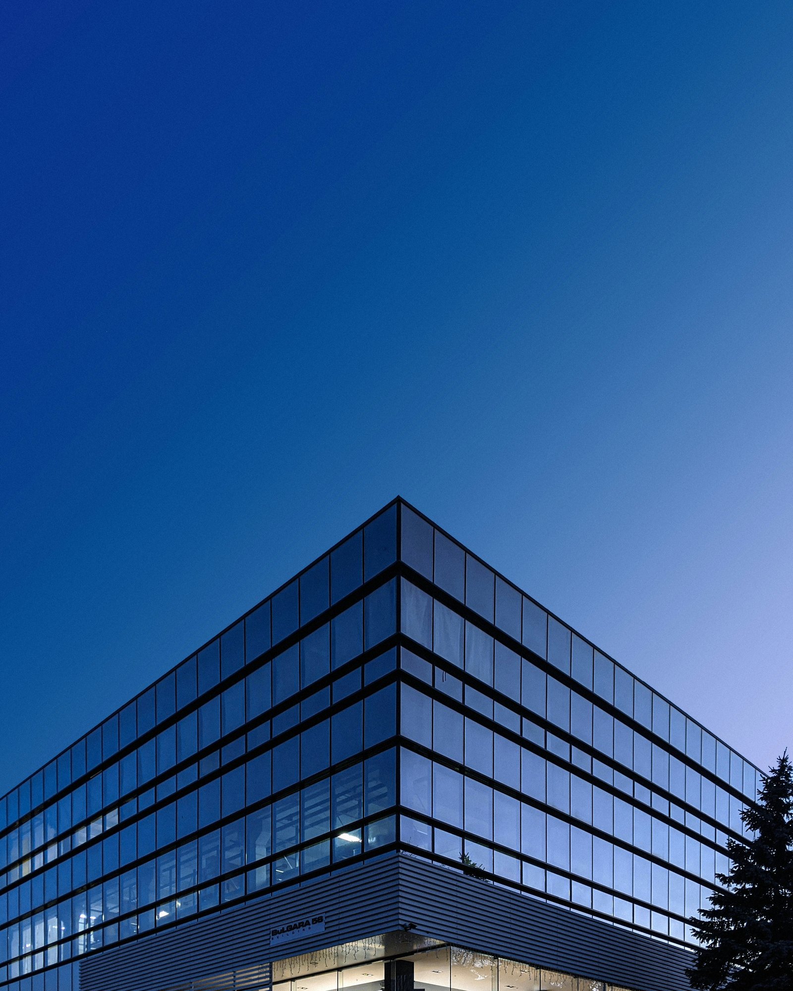 A modern glass office building against a deep blue evening sky